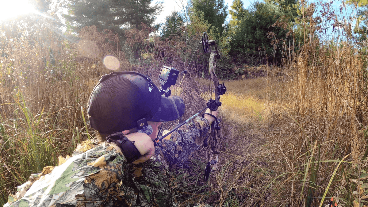Person in camouflage gear with a bow and arrow in a forest setting